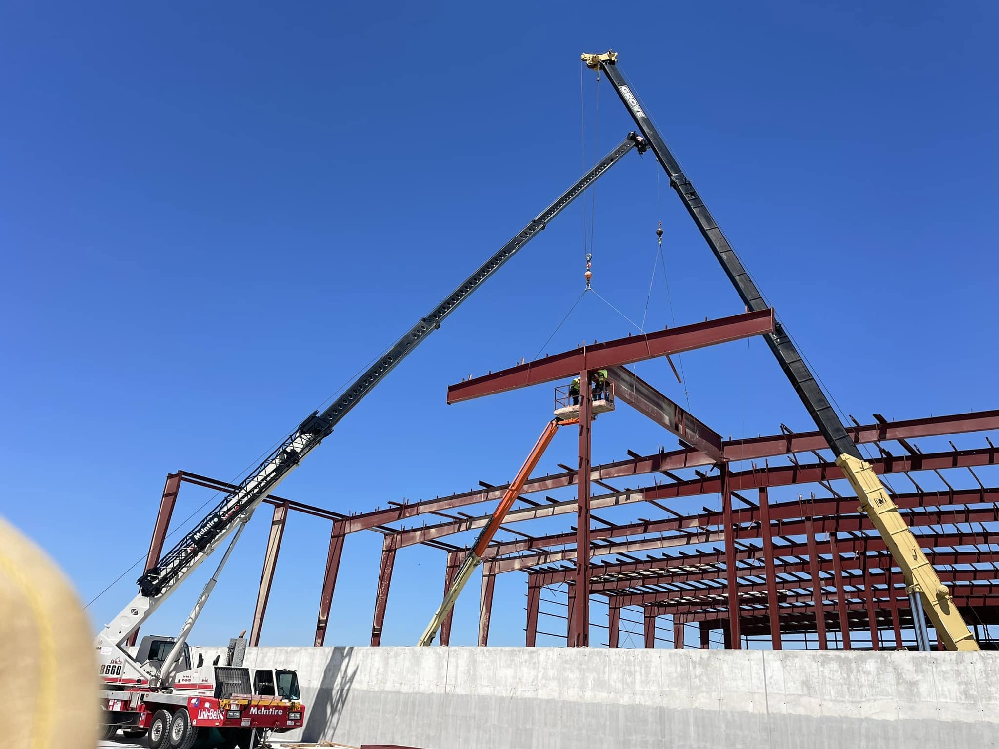 Two cranes setting primary steel beams onto tilt-wall panels at the Fort Worth warehouse