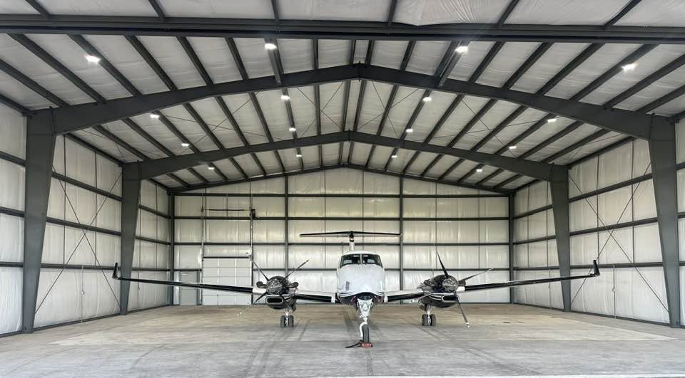 Interior of a clear-span metal aircraft hangar with a turboprop aircraft parked inside